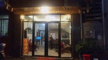 A hotel entrance with a glass door, a red mat, and a signboard.