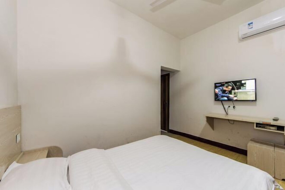 A hotel room with a bed, a TV mounted on the wall, and an air conditioning unit.