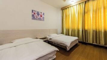Habitación de hotel con dos camas individuales, ventilador de techo, un cuadro en la pared y una ventana con cortinas amarillas.