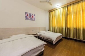A hotel room with two single beds, a ceiling fan, a painting on the wall, and a window with yellow curtains. - Anping Hotel (Wuyishan)