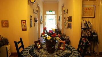 Uma área de refeições com uma mesa redonda, cadeiras e um vaso de flores. Há relógios fixados na parede e quadros emoldurados.