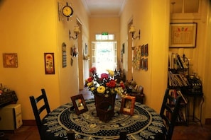 A dining area with a round table, chairs, and a vase of flowers. There are wall-mounted clocks and framed pictures. - Chuanwu Old Villa Family Hotel (Xiamen)