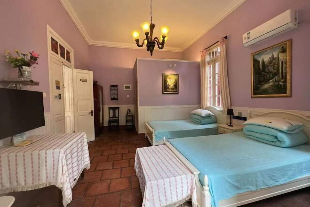 A bedroom with two beds, a chandelier, a television, and a painting on the wall.