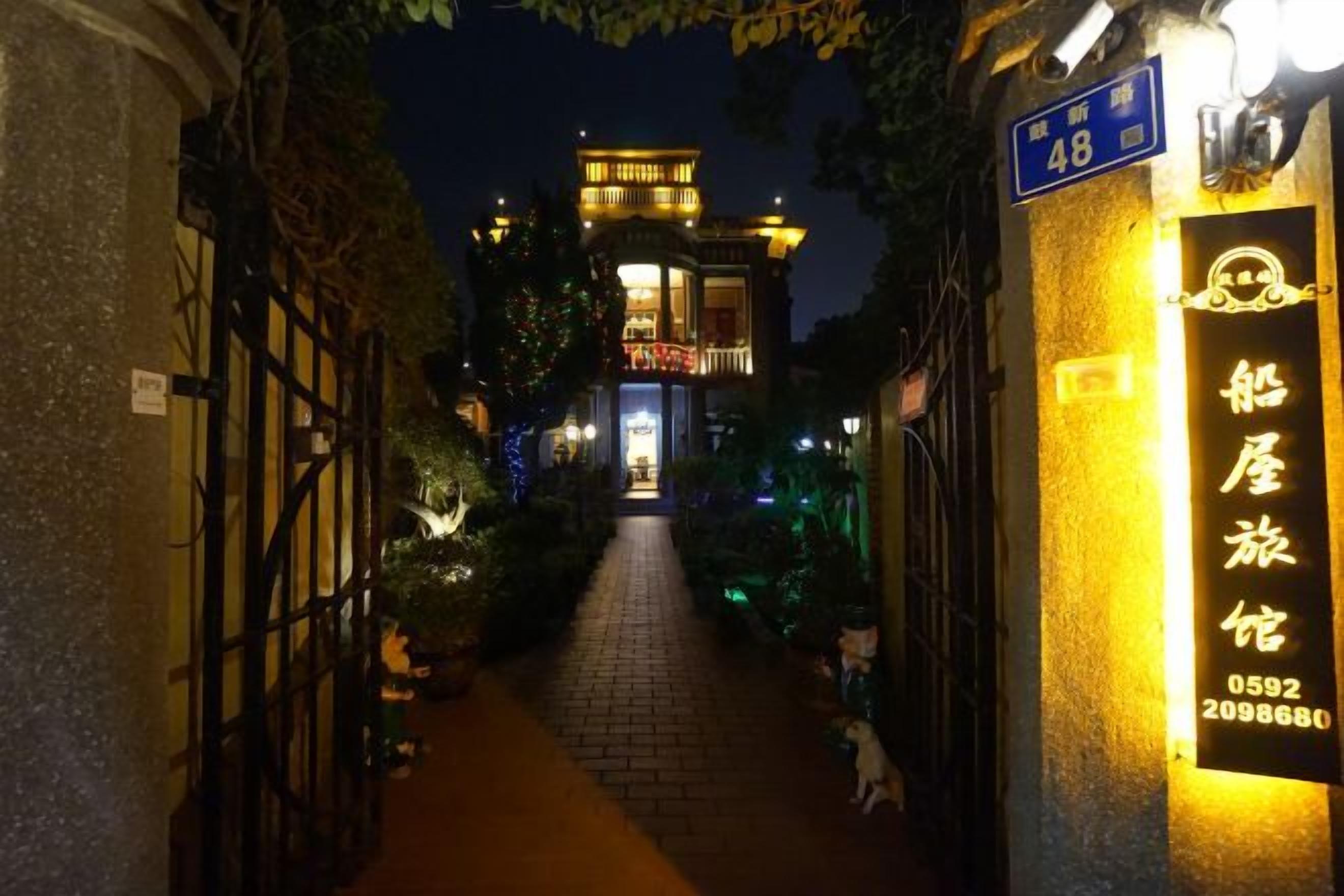 A nighttime view of a narrow alleyway leading to a building with illuminated signage and a traditional architectural style.