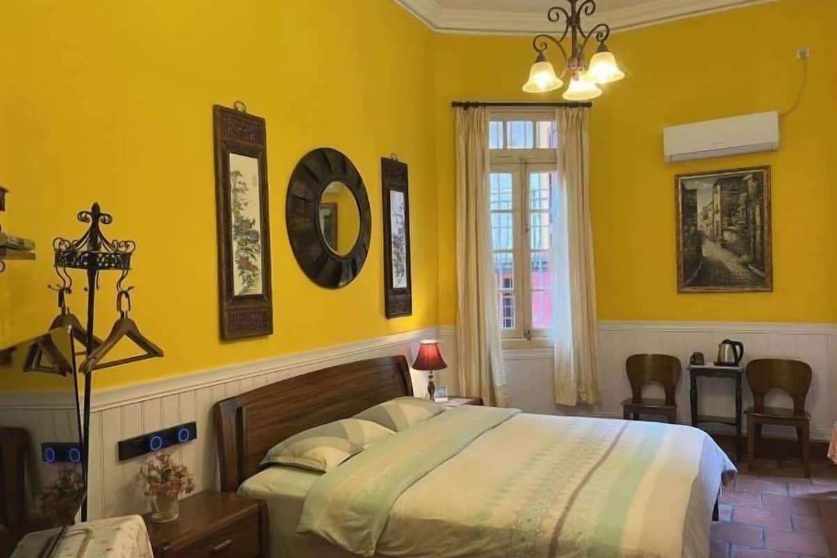 A room with a bed, a nightstand, a lamp, a mirror, and a window with curtains.