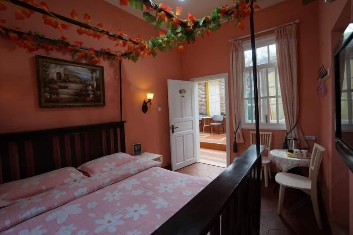 A bedroom with a bed, a chair, a table, a painting, and a door leading to a balcony.