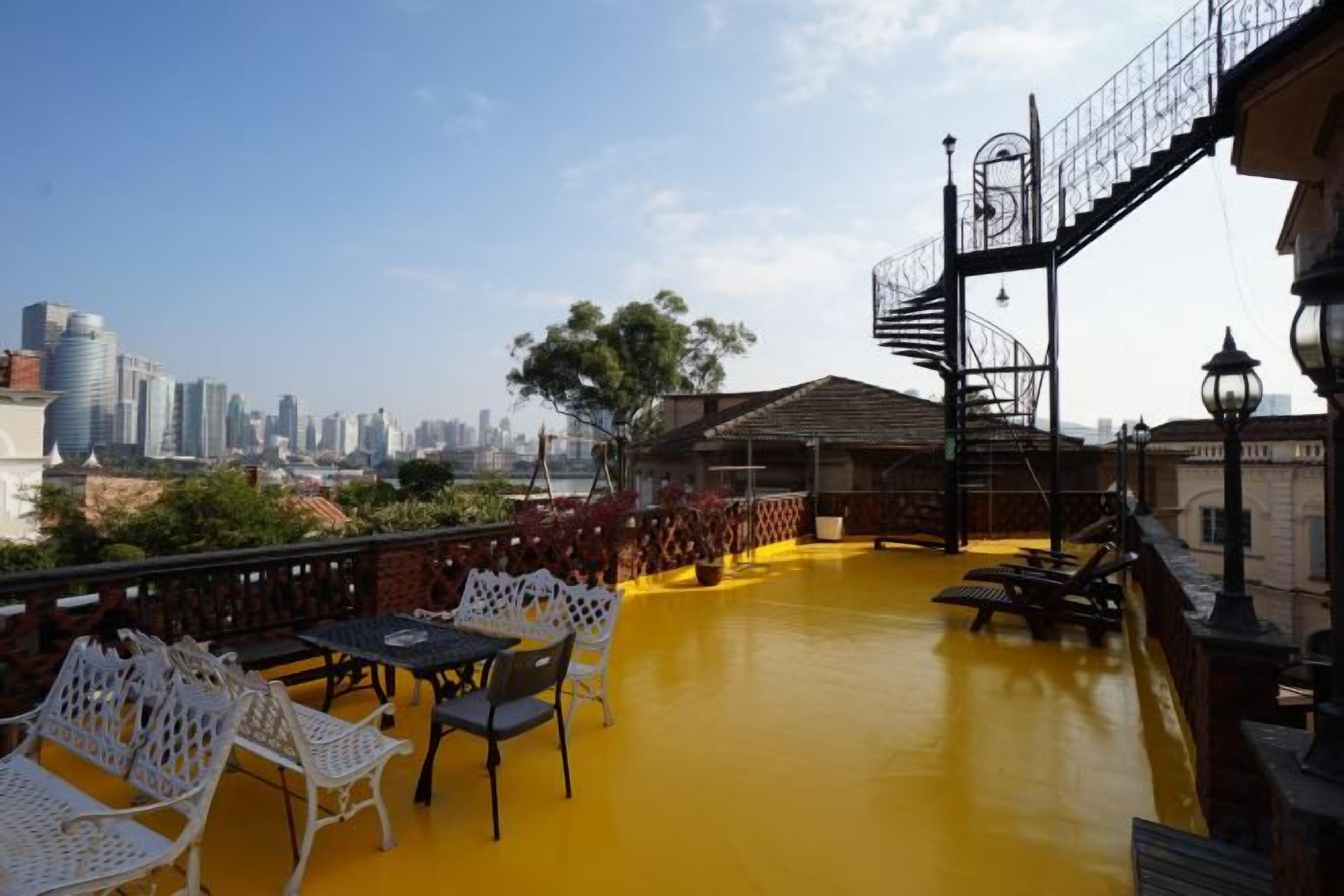 Una terraza en la azotea con mobiliario exterior, vista al horizonte de la ciudad y una escalera que lleva a un nivel superior.