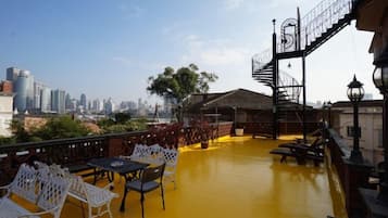 Una terraza en la azotea con mobiliario exterior, vista al horizonte de la ciudad y una escalera que lleva a un nivel superior.