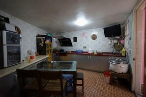 A kitchen with a glass table, chairs, a refrigerator, a sink, and a television mounted on the wall. - Chuanwu Old Villa Family Hotel (Xiamen)