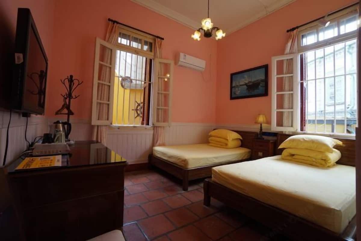 A room with two beds, a desk, a chair, a television, and a window with curtains.