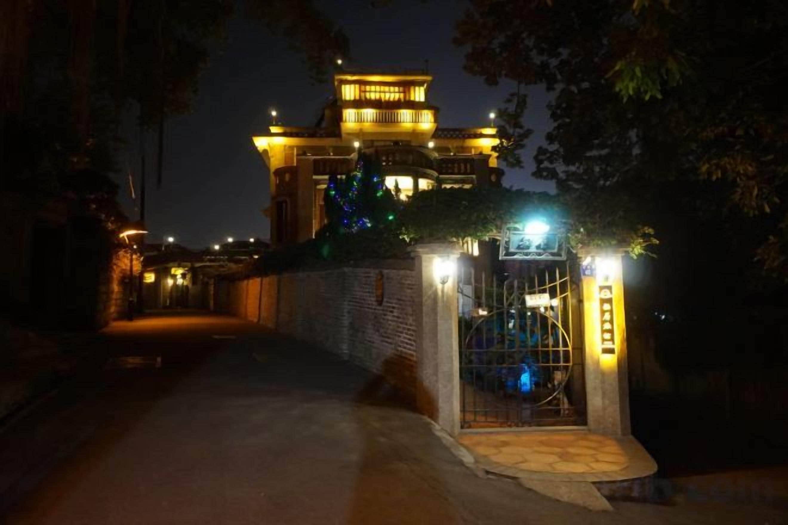 A pathway leading to a building with a traditional architectural style, a gated entrance, and illuminated signage.