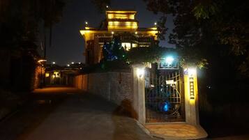 A pathway leading to a building with a traditional architectural style, a gated entrance, and illuminated signage.