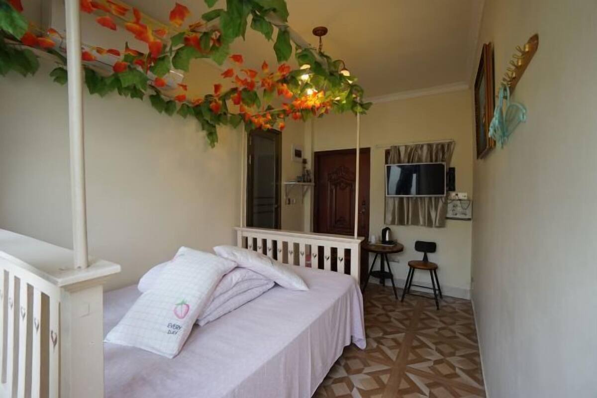 A bedroom with a bed, a small table, a chair, and a decorative plant.