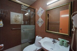 Un baño con cabina de ducha de vidrio, inodoro blanco, lavamanos con espejo y teléfono.