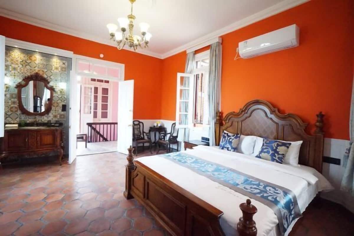 A bedroom with a large bed, a wooden headboard, a chandelier, a dresser, and a mirror.