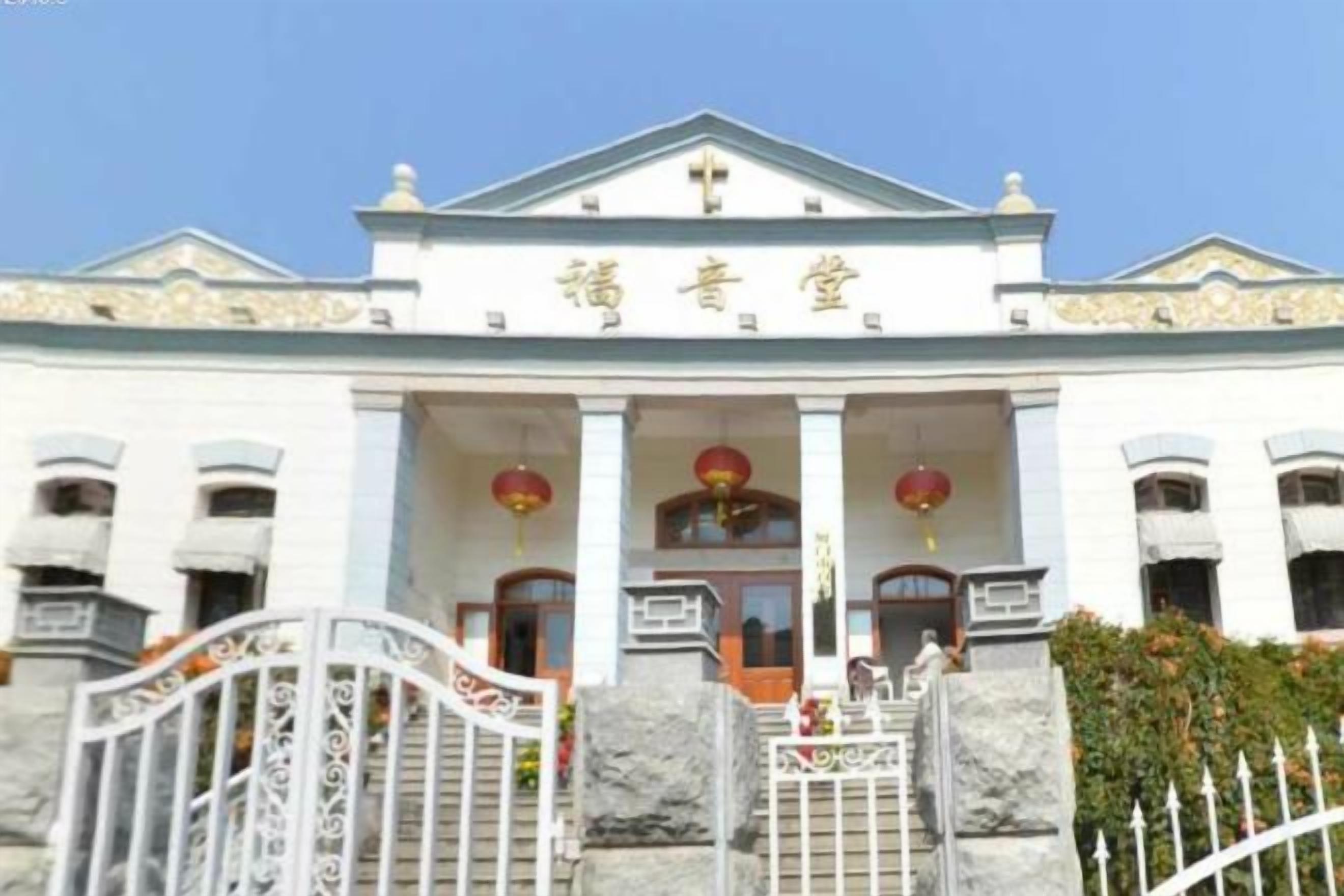 A building with a white facade, a central entrance with columns, and a gated entrance.