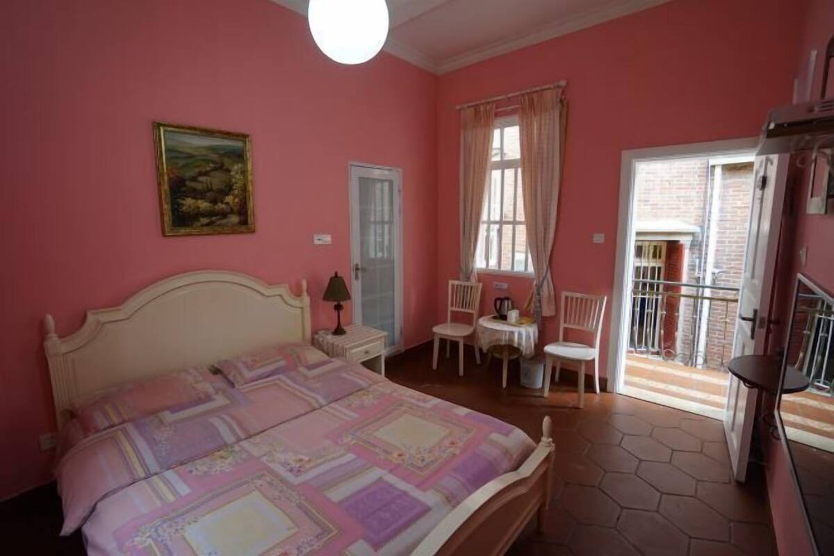 A bedroom with a large bed, a desk, a chair, and a window with curtains.