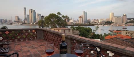 A table with a bottle and glasses on a terrace overlooking a cityscape.