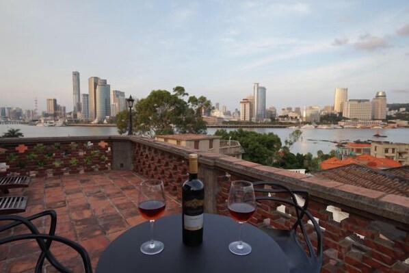 Una mesa con una botella y vasos en una terraza con vistas a un paisaje urbano.