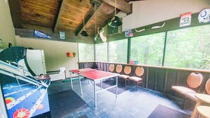 Una habitación con mesa de ping pong, sillas, un refrigerador y una ventana que da a vistas de árboles.