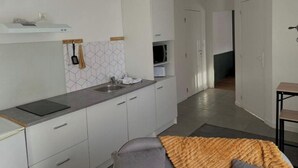 A modern kitchen with white cabinets, a grey countertop, and a microwave. There is a window with a view of the outside. - Le Quai des Marins (Châteauroux)