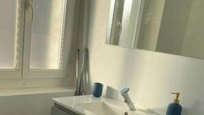 A bathroom with a white sink, a mirror above it, and a patterned floor. - Le Quai des Marins (Châteauroux)