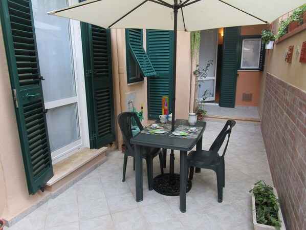 A patio with a table and chairs, a small plant, and a window with shutters.