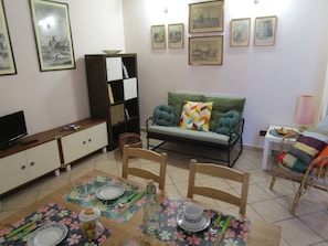 A living room with a sofa, dining table, chairs, and a television.