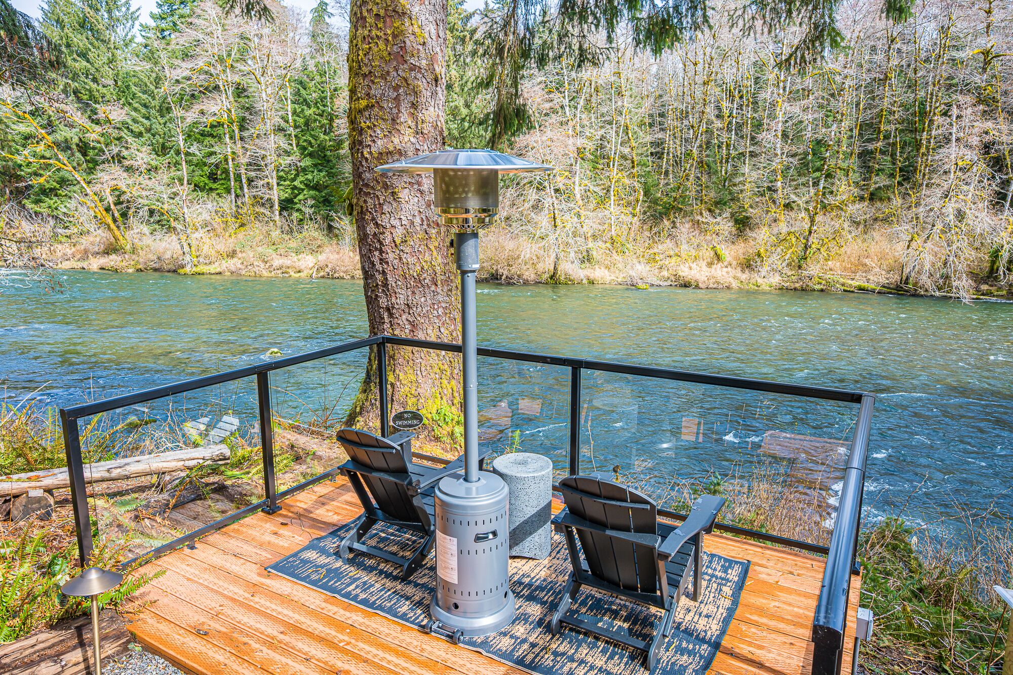 A deck with outdoor seating and a wood-burning stove, overlooking a river.