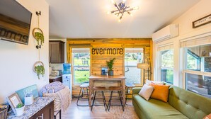 Un intérieur chaleureux avec un mur en bois, un canapé vert, un coin repas et un luminaire suspendu au plafond.
