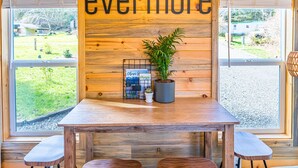 Un intérieur en bois avec une table et des chaises, une enseigne sur laquelle on peut lire « toujours et à jamais », et une vue sur l’extérieur grâce à de grandes fenêtres.