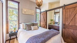 Une chambre à coucher avec un grand lit, une armoire en bois, un lustre et une fenêtre avec des stores.