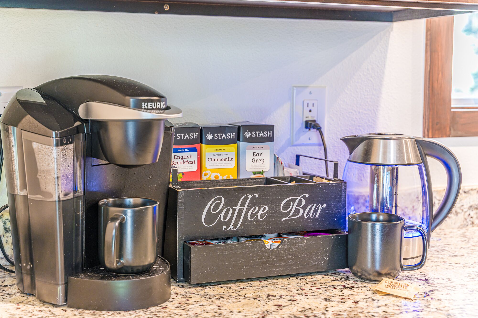 Un espace café aménagé avec une machine Keurig, une cafetière et une boîte étiquetée « Bar à café » contenant divers produits à base de thé et de café.