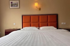 Ein Hotelzimmer mit einem großen Bett, einem Kopfteil, einem Nachttisch, einer Wandlampe und einem gerahmten Bild an der Wand.