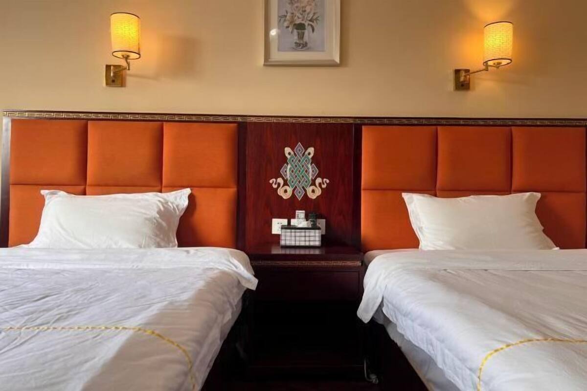Een hotelkamer met twee bedden, elk met witte lakens en een gele rand. Aan weerszijden van de bedden hangen wandlampen.