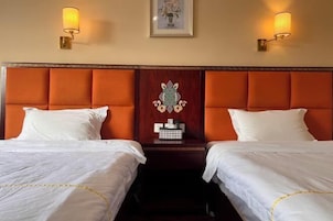 Habitación de hotel con dos camas, cada una con ropa de cama blanca y ribete amarillo. Hay lámparas fijadas en la pared a cada lado de las camas.