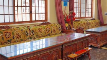 A traditional room with a long wooden table, a sofa with floral upholstery, and a window with wooden frames.