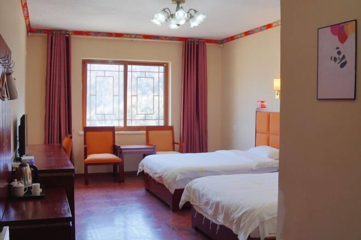 Een hotelkamer met twee bedden, een bureau, een stoel en een raam met gordijnen.