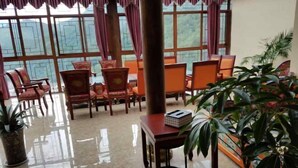 A room with a large window, wooden chairs, a table with a box, and potted plants. - Dawagengzha Ecological Theme Hotel (Baoxing)