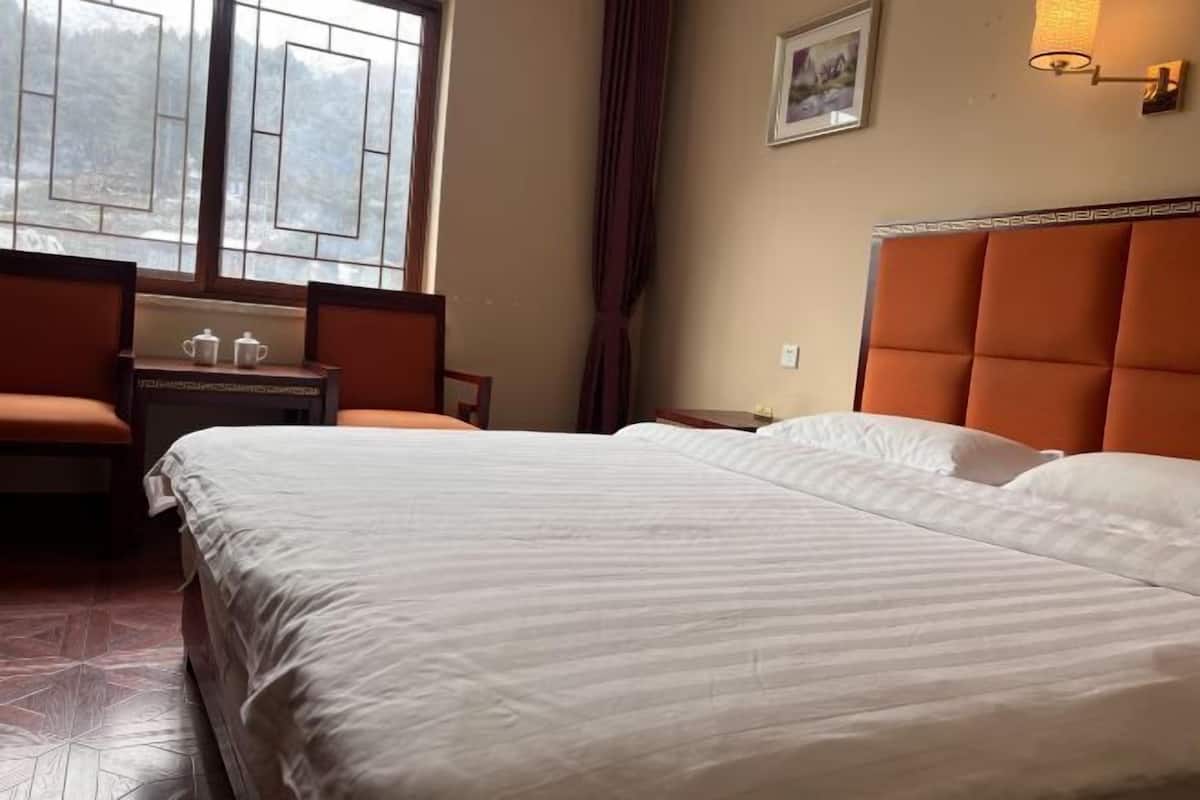 Hotelkamer met een groot bed, een bureau met stoel, een raam met gordijnen en een wandlamp.