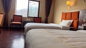 A hotel room with two beds, a desk, and a chair. There is a window with a view of mountains. - Dawagengzha Ecological Theme Hotel (Baoxing)