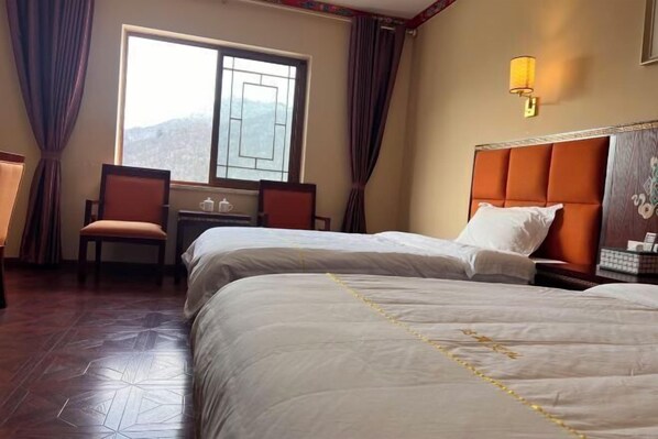 Ein Hotelzimmer mit zwei Betten, einem Schreibtisch und einem Stuhl. Ein Fenster bietet Blick auf Berge.