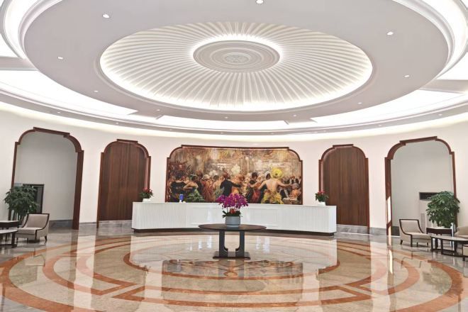 A hotel lobby with a reception desk, seating area, and a large mural on the wall.