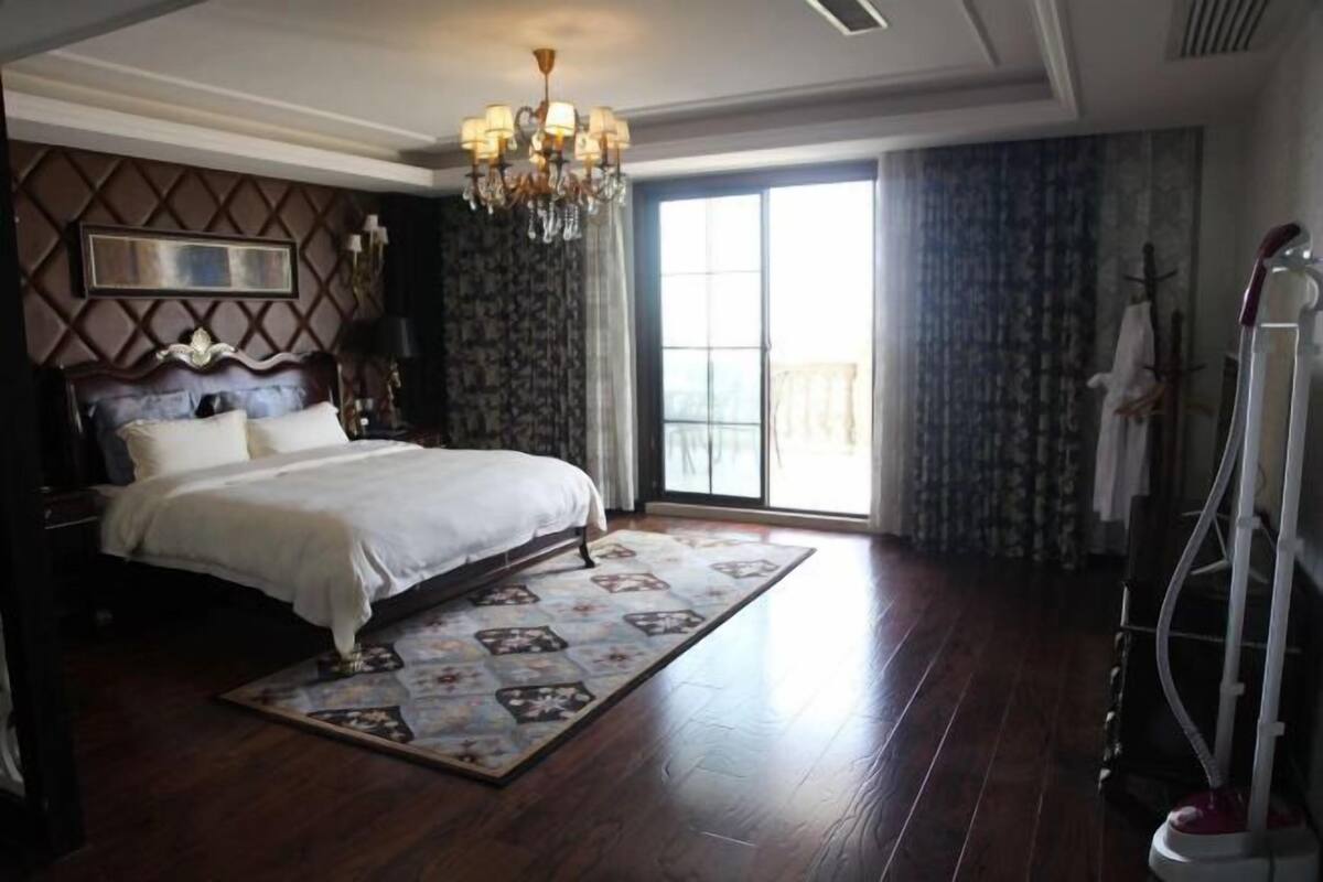 Une chambre spacieuse avec un grand lit, un lustre et une vue sur l’extérieur.