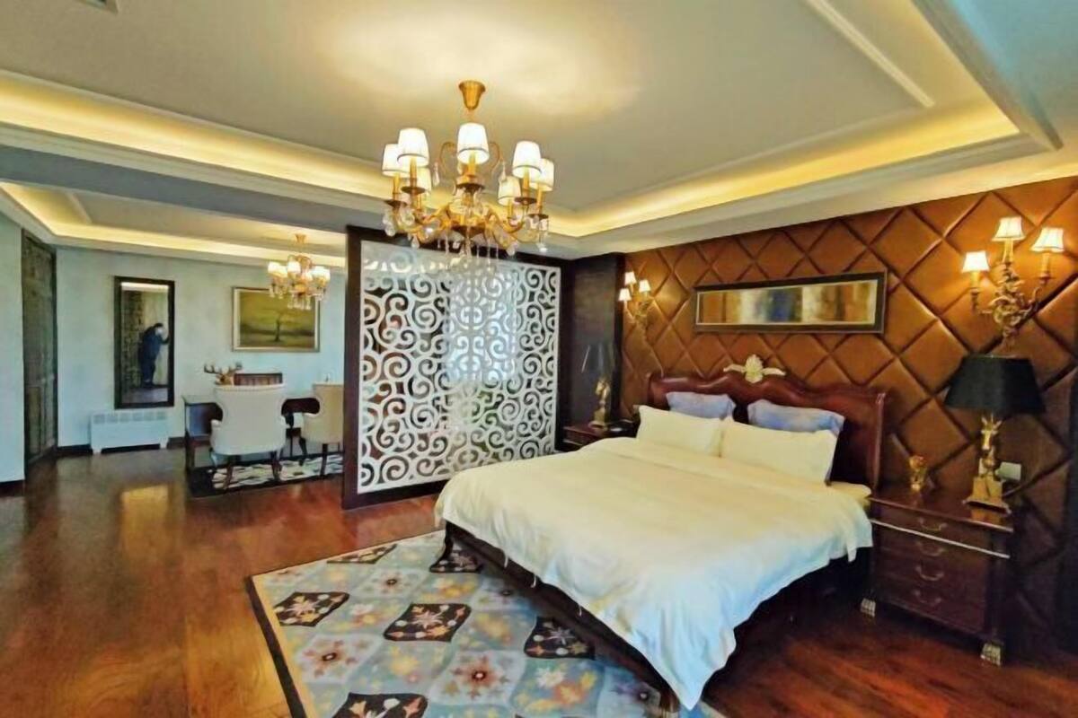 Une chambre spacieuse avec un grand lit, un lustre, un panneau décoratif au mur et une table de chevet avec des lampes.