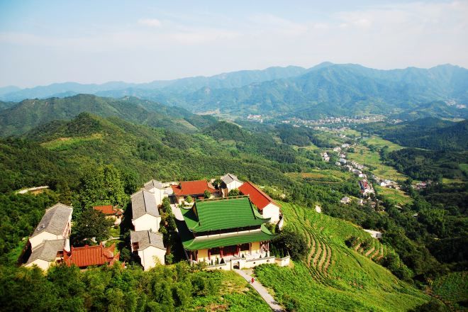 A traditional building with a green roof amidst lush green hills and a valley.