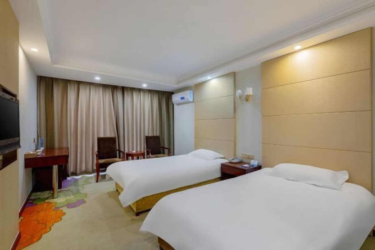 A hotel room with two beds, a desk, a chair, a TV, and a window with curtains.