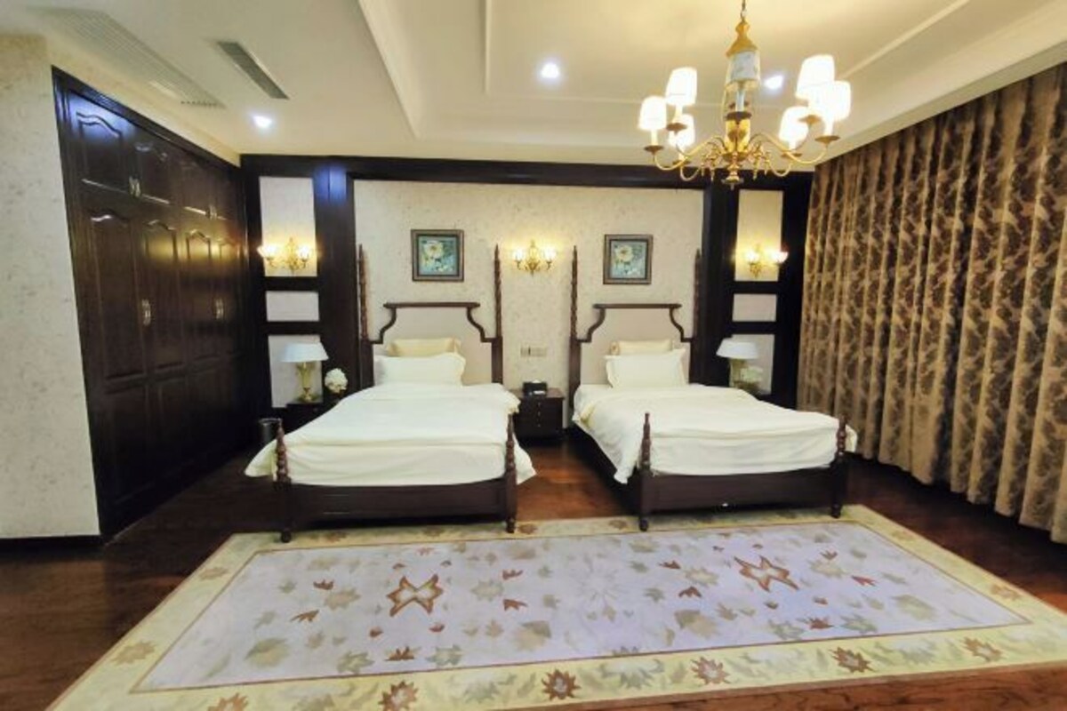 A double room with two beds, a chandelier, a patterned rug, and a large mirror.