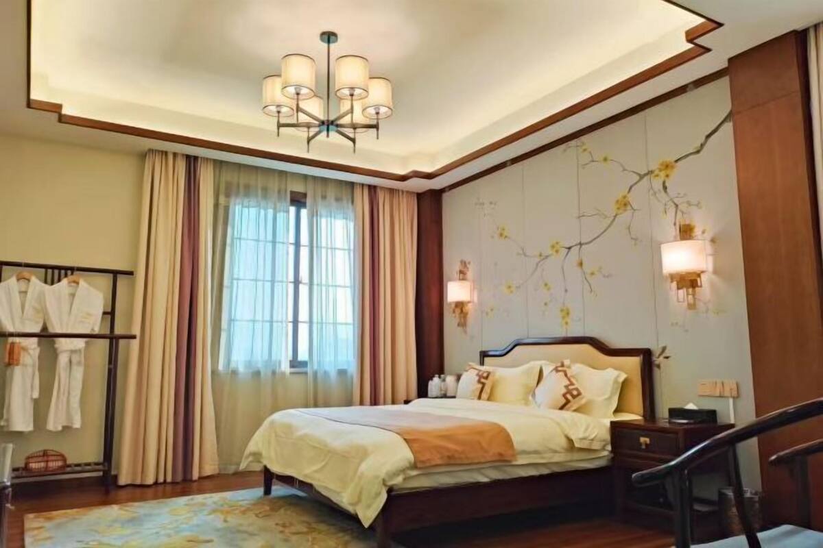 Une chambre d’hôtel avec un grand lit, un lustre, une armoire et une fenêtre avec des rideaux.