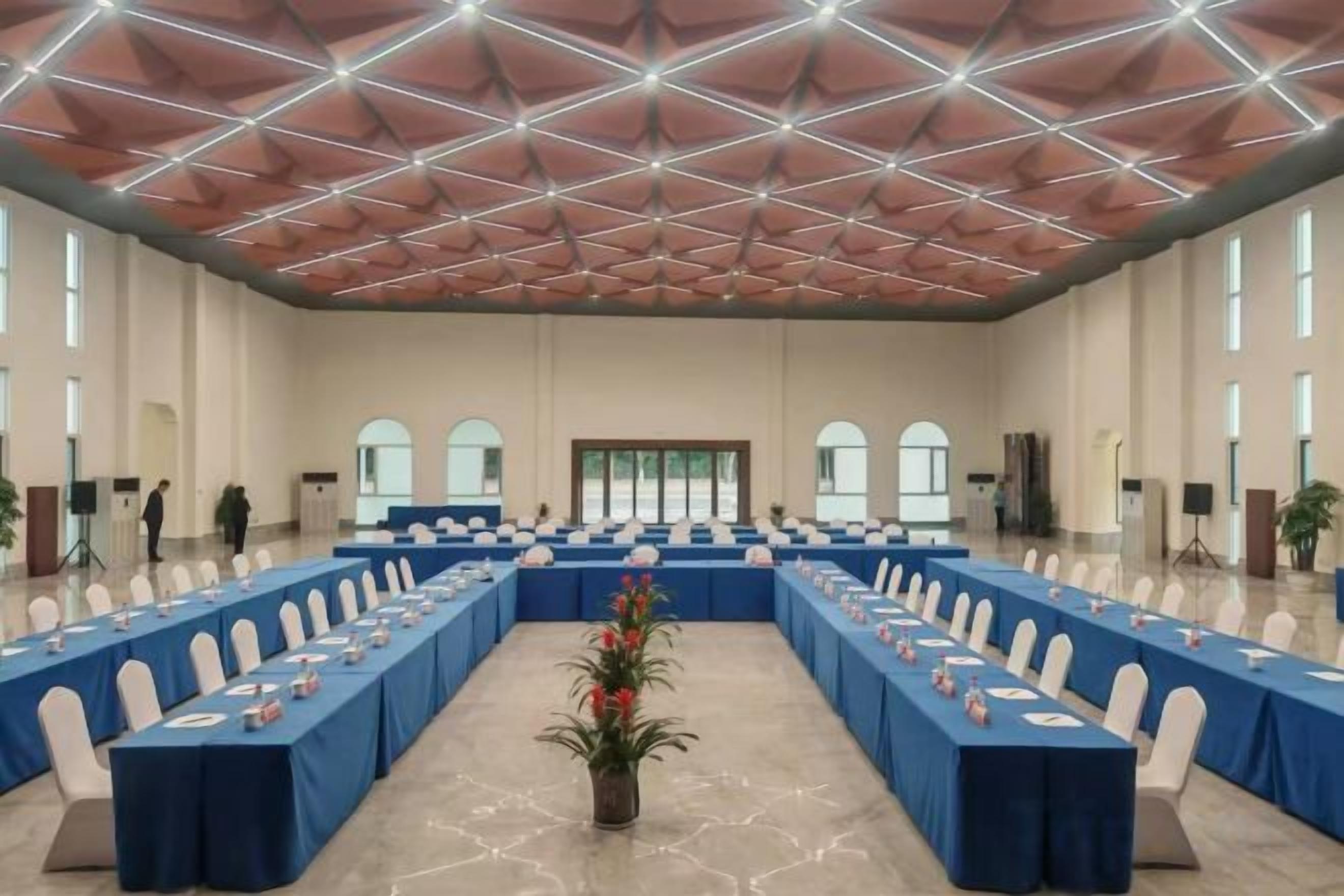 Ein großer Konferenzraum mit einem langen Tisch, Stühlen und einer Decke mit geometrischem Muster.